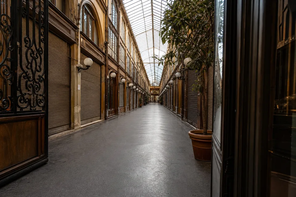 Empty glass-roofed shopping arcade in early morning with closed storefront shutters