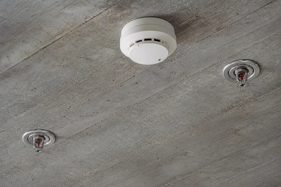 Smoke detector and sprinkler heads on a bare concrete ceiling