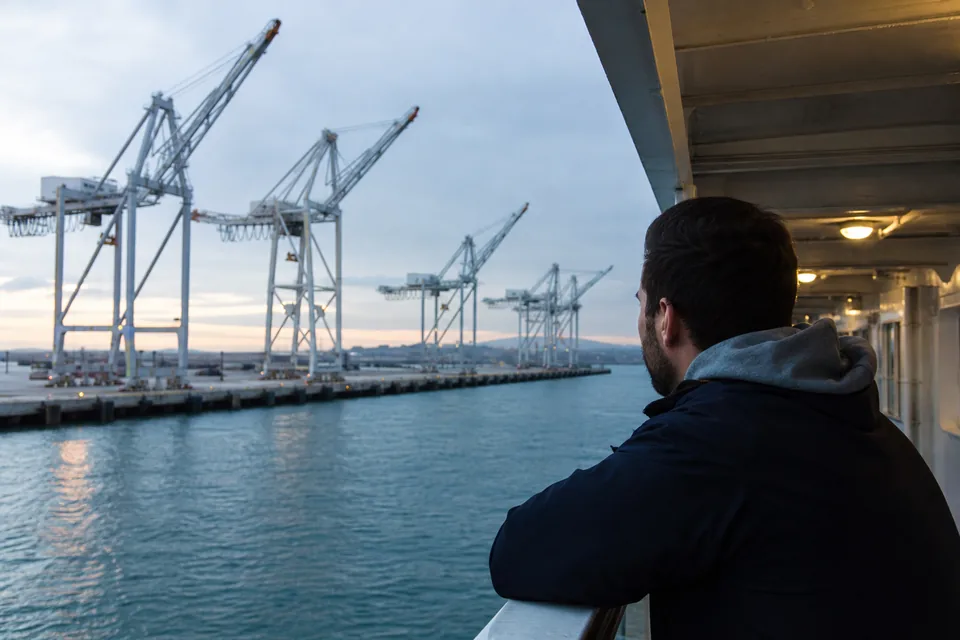 Container port at dawn with a row of gantry cranes, seen over the shoulder of a man at a window