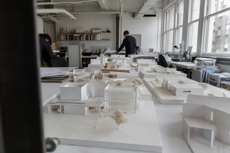Long white tables with many separate building models in a bright studio