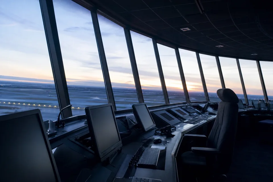 Empty airport control tower cab with tilted panoramic windows over the runways at dawn