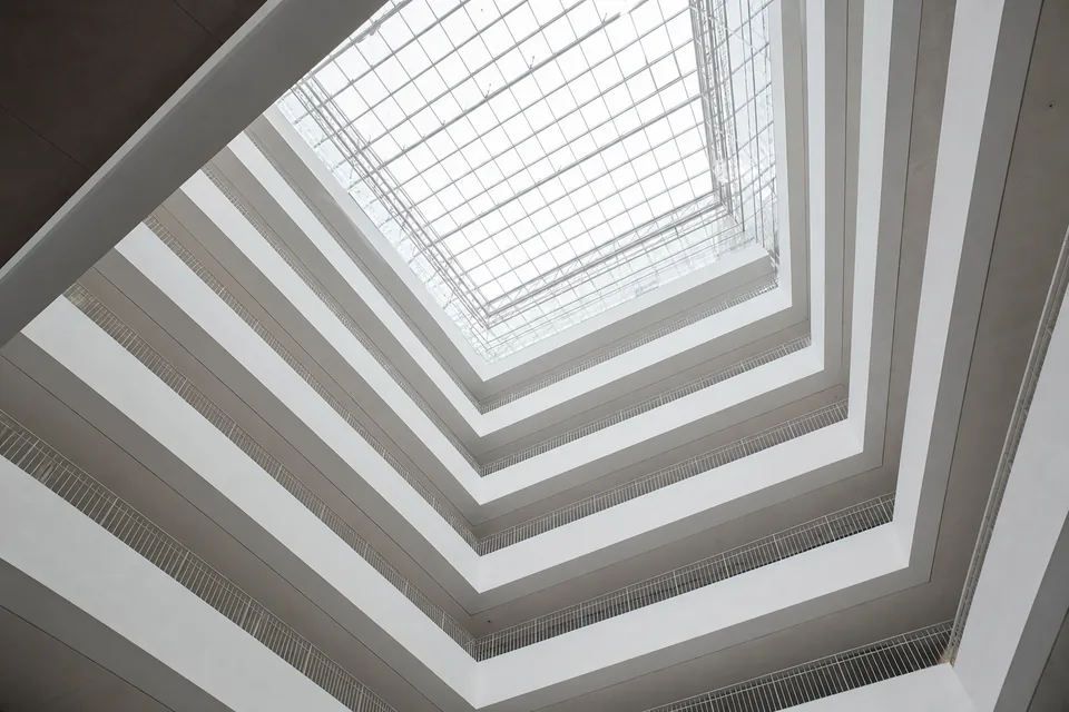 Bright empty multi-level atrium with stacked white balconies and walkways under a glass roof