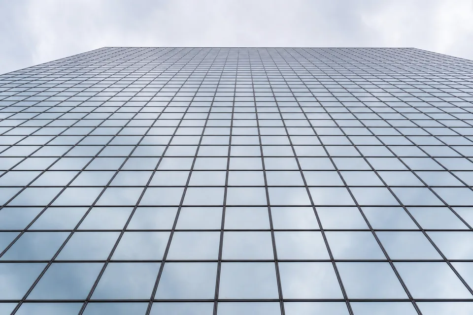 Glass curtain wall of a tall building reflecting a pale morning sky, steel mullions in a regular grid